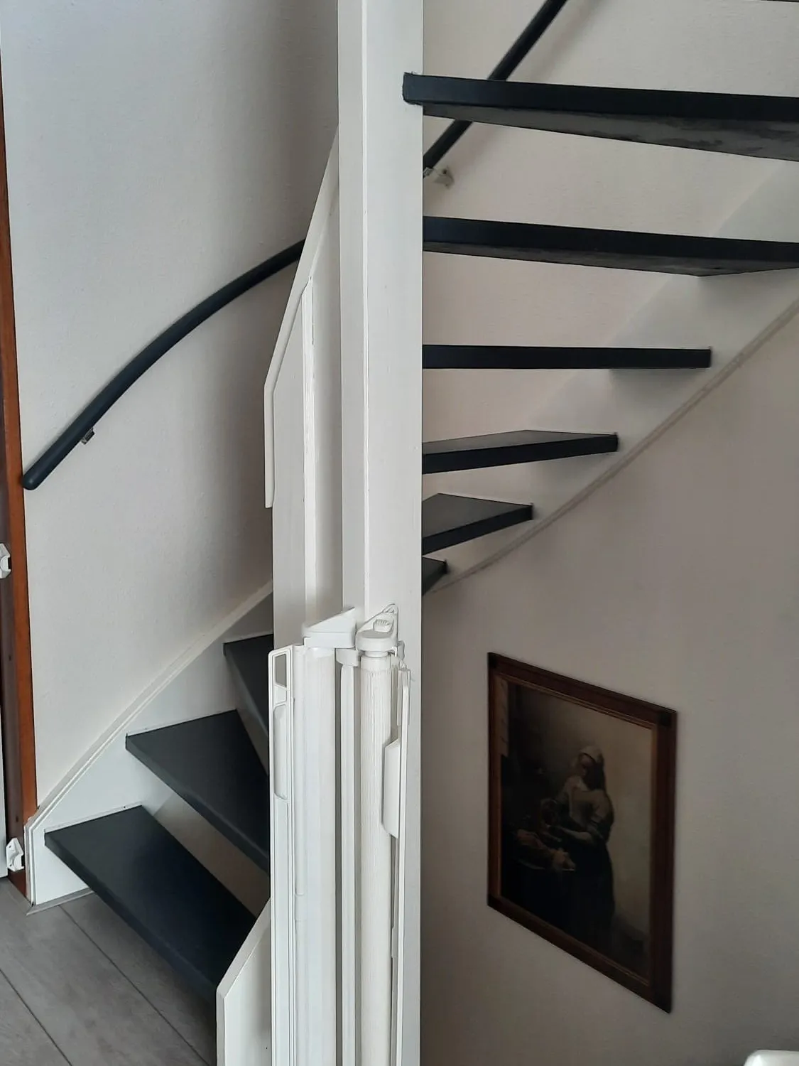 Trap met donker gelakte treden en wit geschilderd houtwerk, met een opgeklapte traplift ernaast