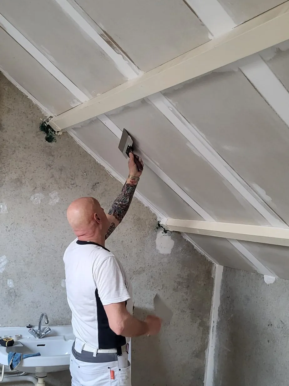 Schilder werkt met een spaan de naden tussen de dakplaten af