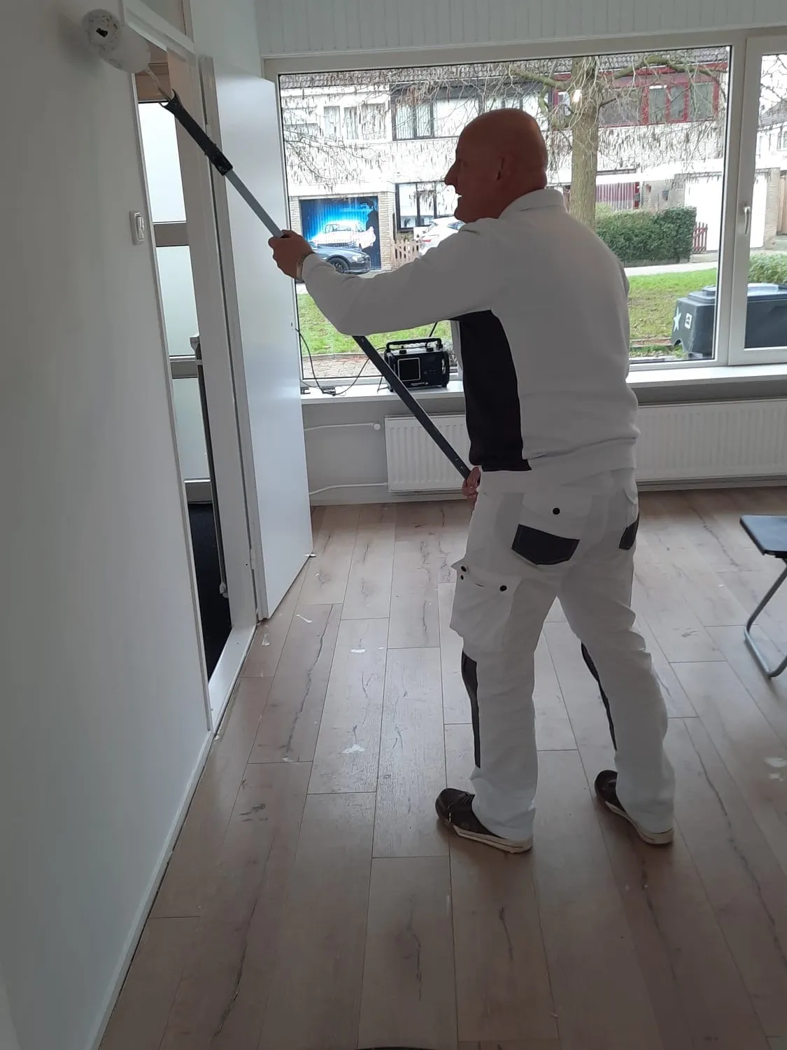 Schilder rolt met een verlengstok een wand in een woonkamer