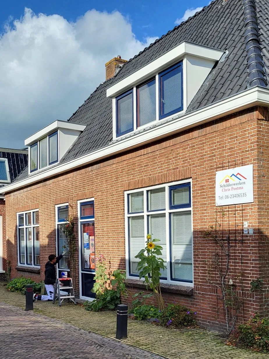 Bakstenen woonhuis aan een straat, met wit geschilderde kozijnen en dakkapellen