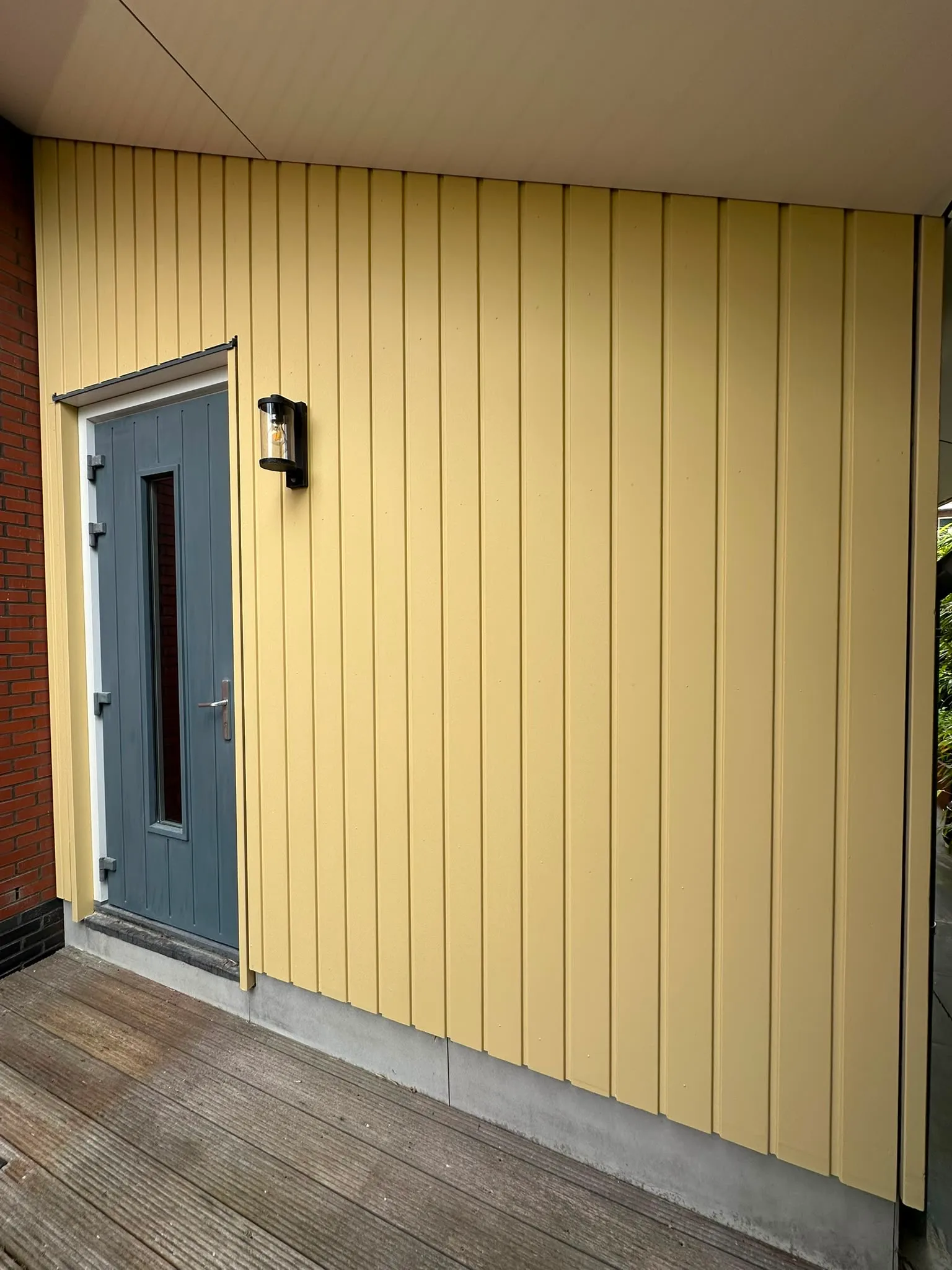 Geel geschilderde verticale gevelbekleding met een grijze voordeur